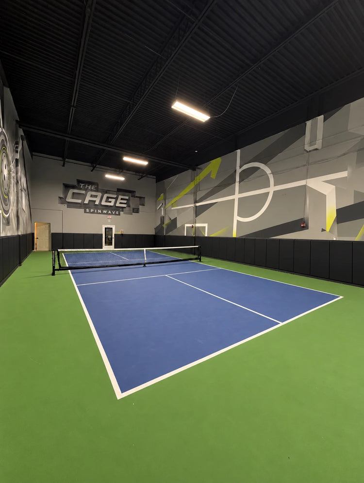The Cage at Spinwave Boca: a full indoor pickleball court with padded walls, the net up and The Cage sign on the far wall