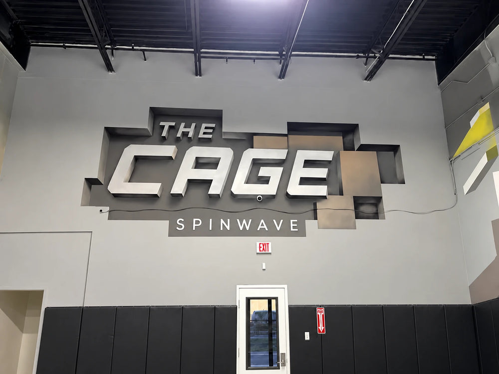 The Cage sign at Spinwave Boca: big three-dimensional letters reading THE CAGE SPINWAVE above the court door and padded walls