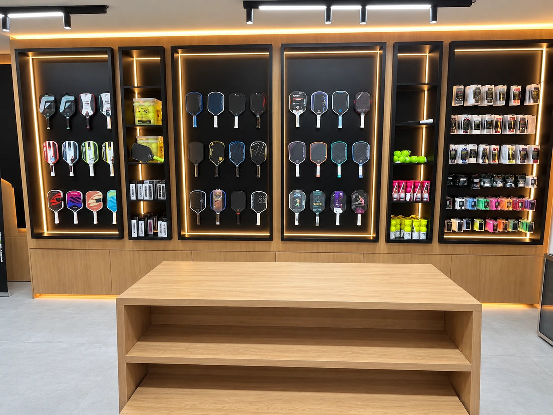 The paddle wall at Spinwave Boca: demo paddles in lit black display cases, with balls, grips and overgrips on the shelves between them