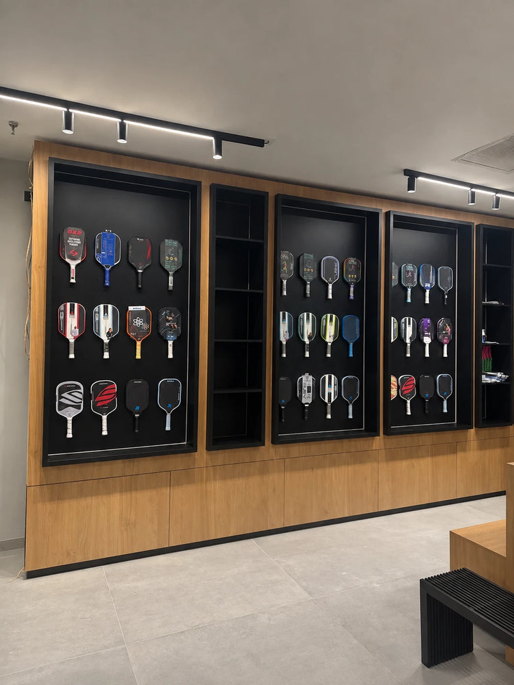 The paddle wall at Spinwave Boca: demo paddles hung in lit black display cases set into wood cabinetry